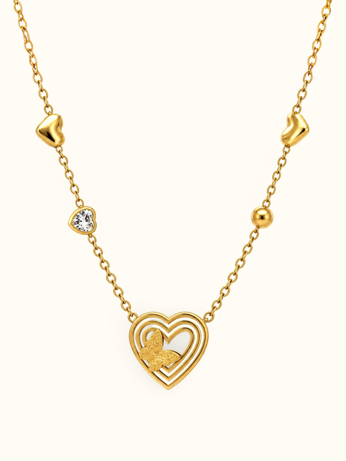 Gold-toned necklace featuring a layered open-heart pendant with a textured butterfly detail, a sparkling heart accent and polished heart-shaped elements along the chain.

Close-up of a delicate gold heart and butterfly necklace displayed against a clean white background.
