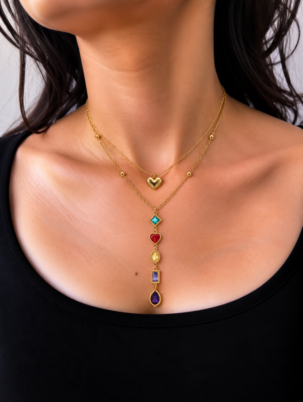 Gold-toned layered necklace with a glossy heart charm and a cascading pendant featuring blue, red, yellow and purple stones.
Colourful statement necklace with decorative gold-toned settings and delicate chains worn by a model.