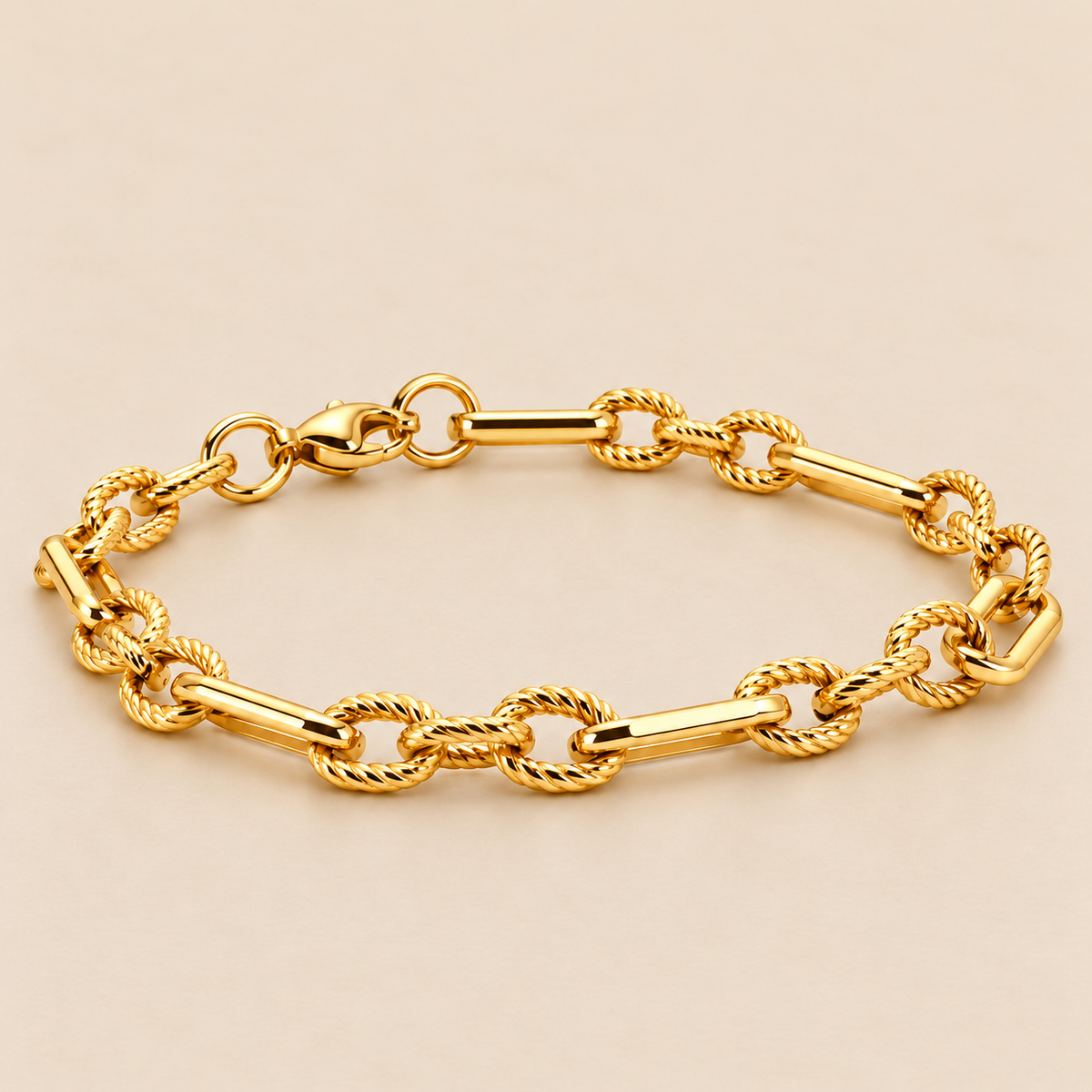 Gold-toned stainless steel chain bracelet featuring twisted rope-style links connected by elongated polished bar links.
Statement link bracelet with a shiny golden finish and lobster clasp, displayed on a clean pink background.