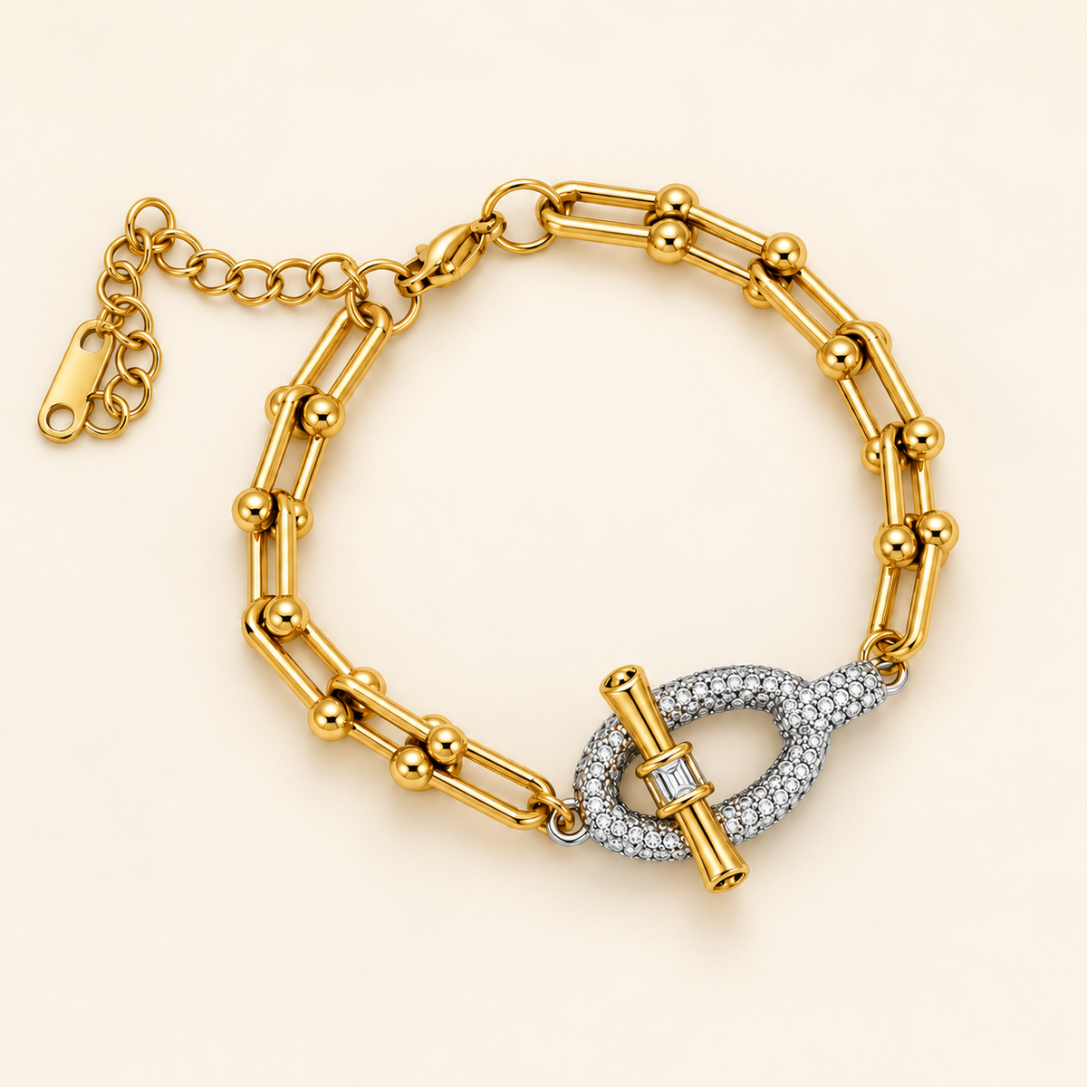 Gold-toned stainless steel bracelet featuring elongated geometric links and a pavé-set oval centrepiece crossed by a polished bar.
Statement bracelet with an adjustable chain and mixed gold-and-silver detailing, displayed on a clean pink background.