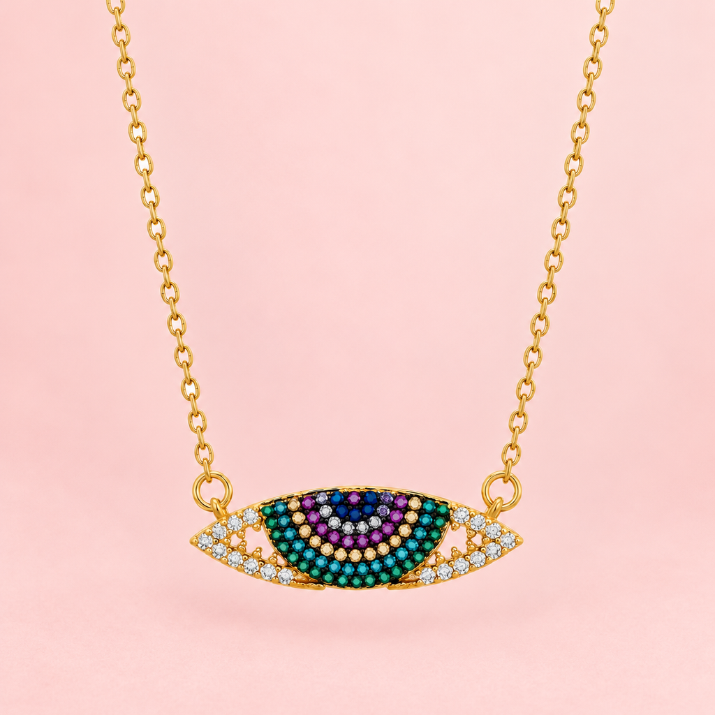 Gold-tone necklace with a horizontal rainbow evil eye pendant featuring multicoloured stones displayed against a pink background.