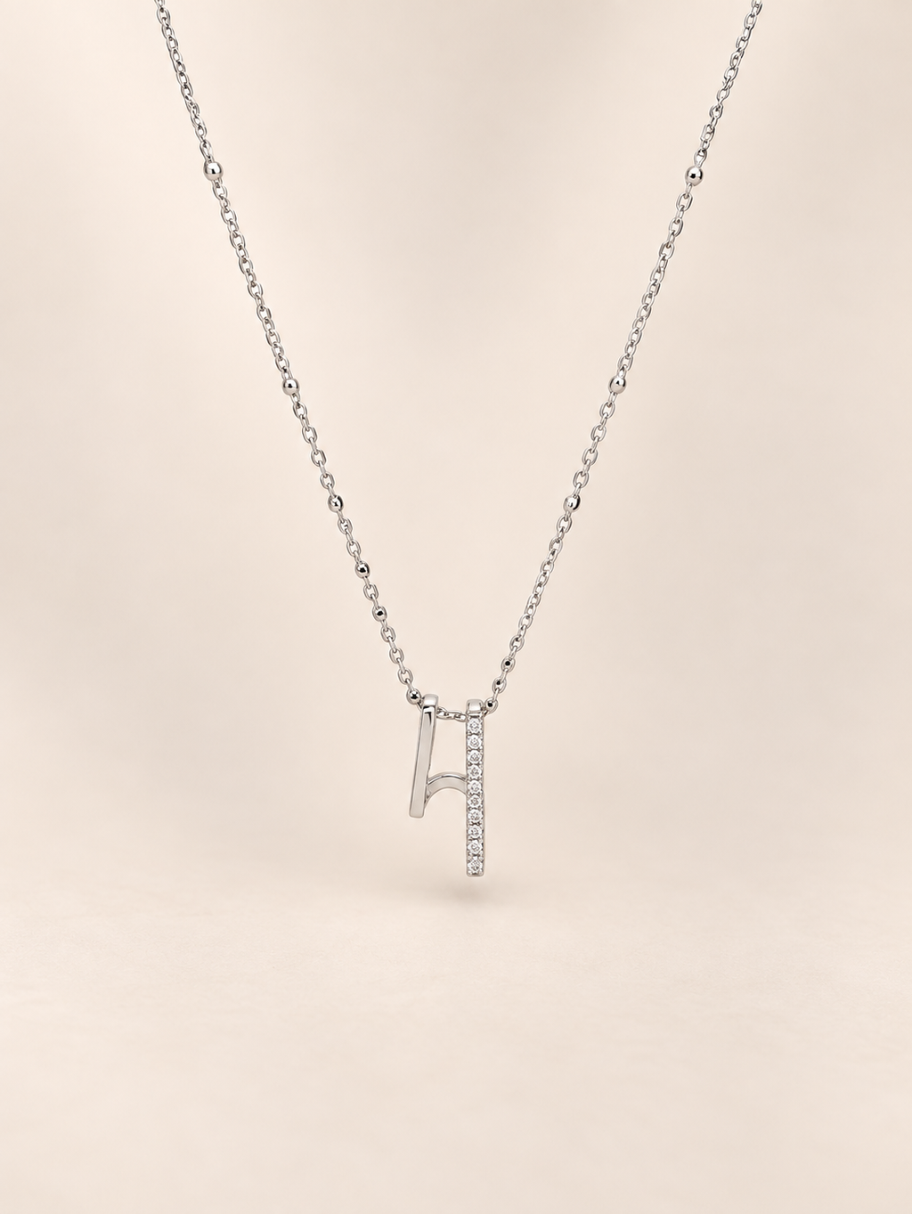 A delicate silver necklace featuring a pendant shaped like a musical noteembellished with small clear stones along one side, set against a solid pale beige background.