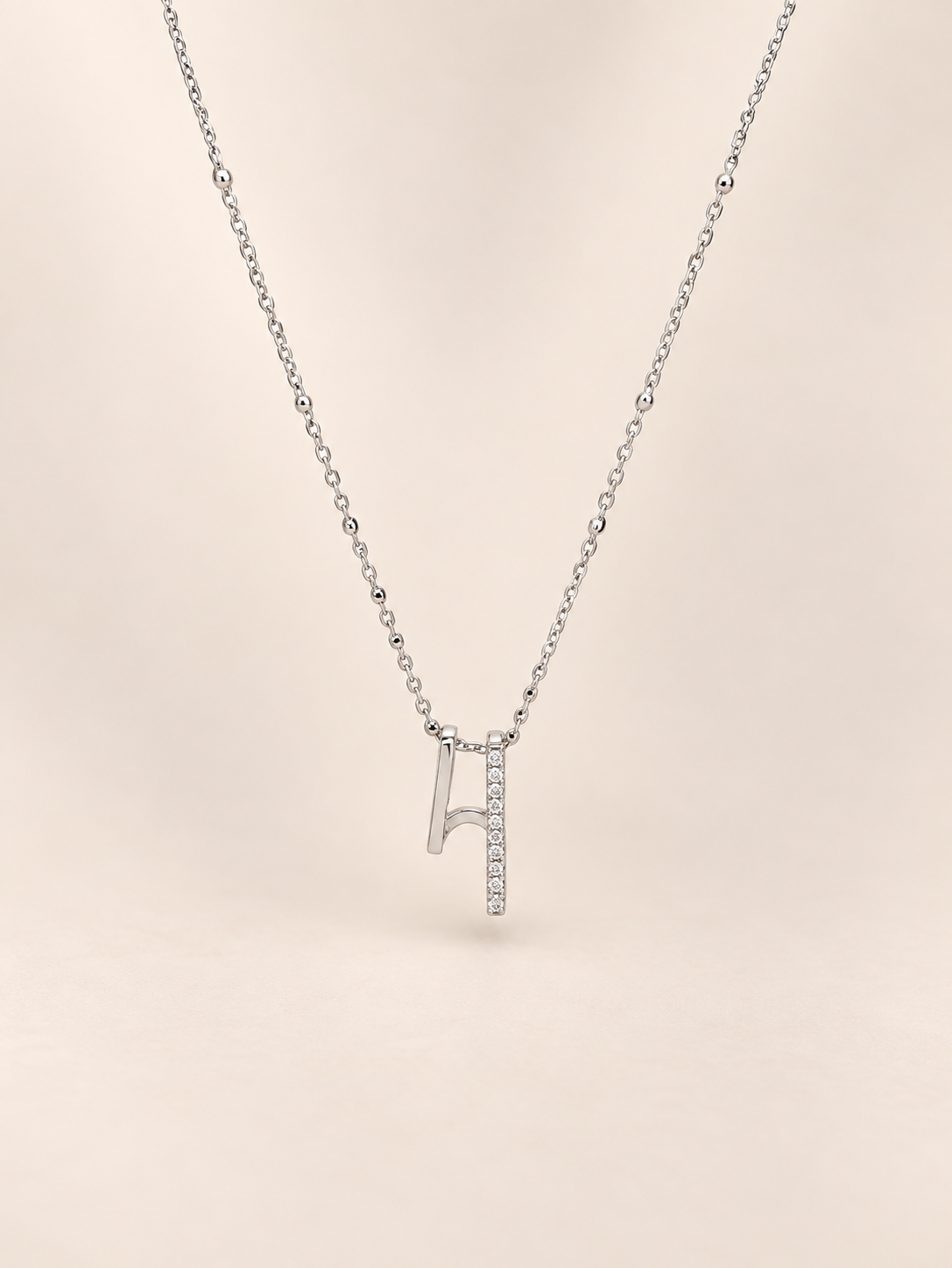 A delicate silver necklace featuring a pendant shaped like a musical noteembellished with small clear stones along one side, set against a solid pale beige background.