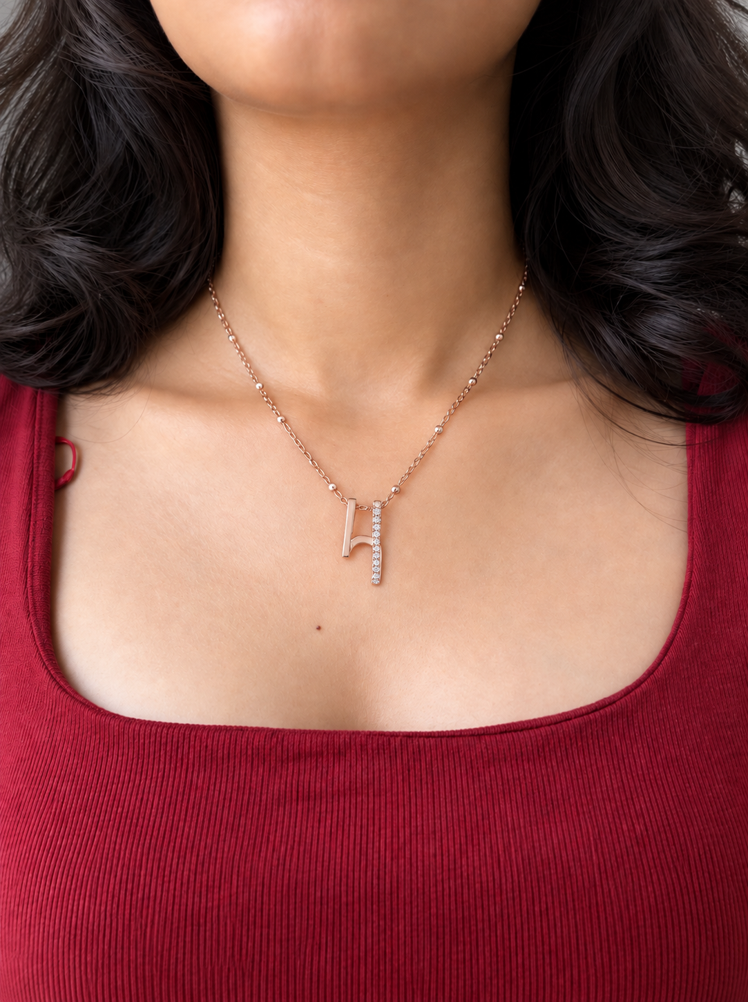 A delicate silver chain necklace featuring a small silver pendant which is a musical note on a model wearing a red colour top.