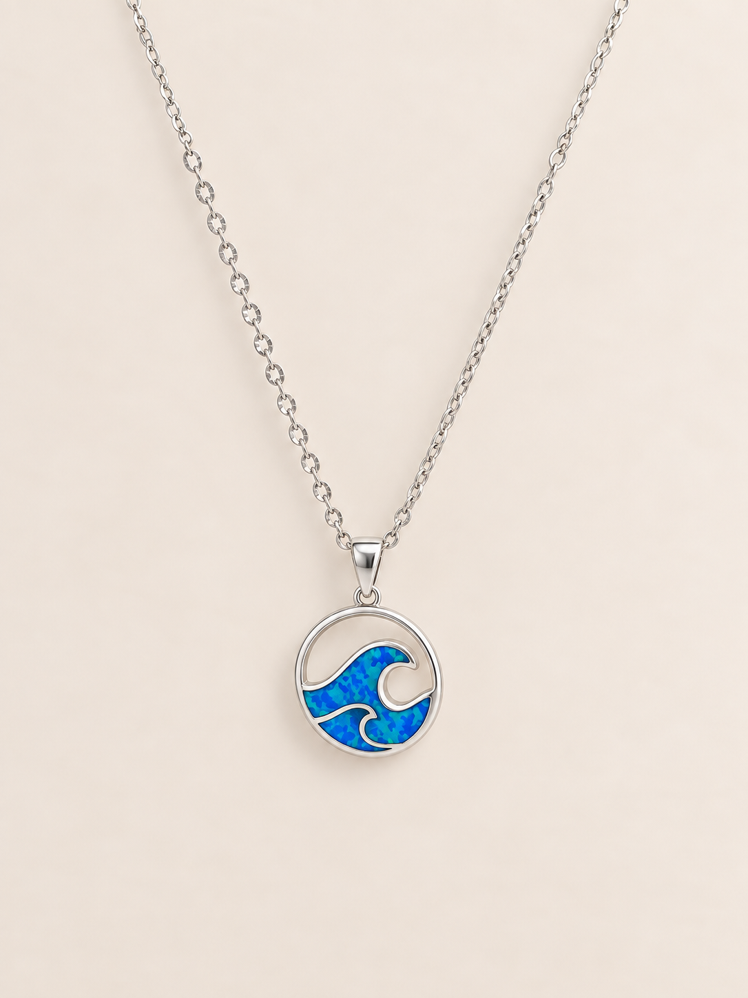 A silver chain necklace with a circular pendant featuring a blue and white wave design, displayed on a light beige background.
