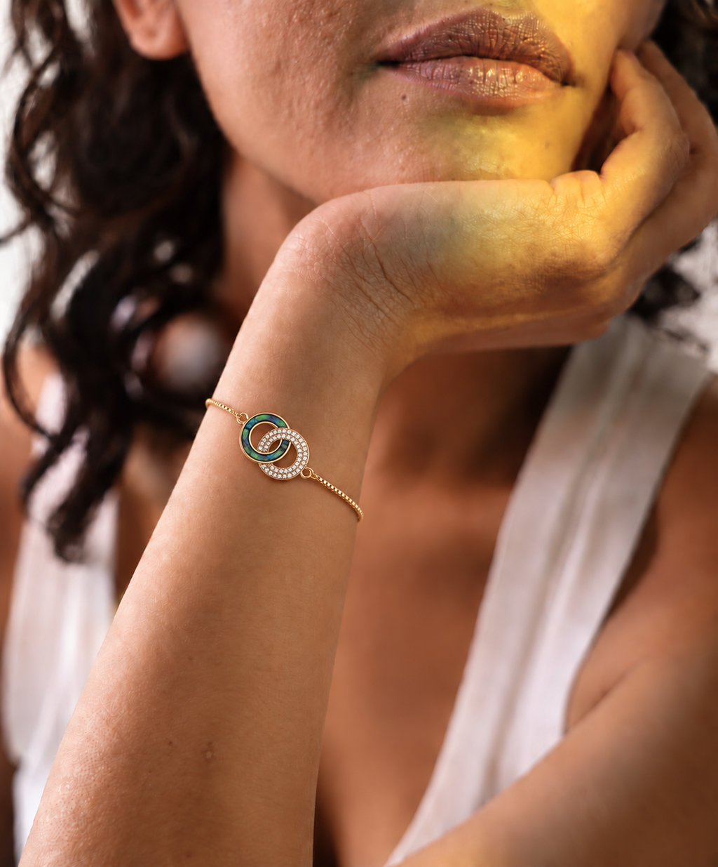 Gold-toned stainless steel bracelet featuring two intertwined circles, one with green enamel and the other set with sparkling white stones.
Delicate chain bracelet with an adjustable slider closure, worn by a model.