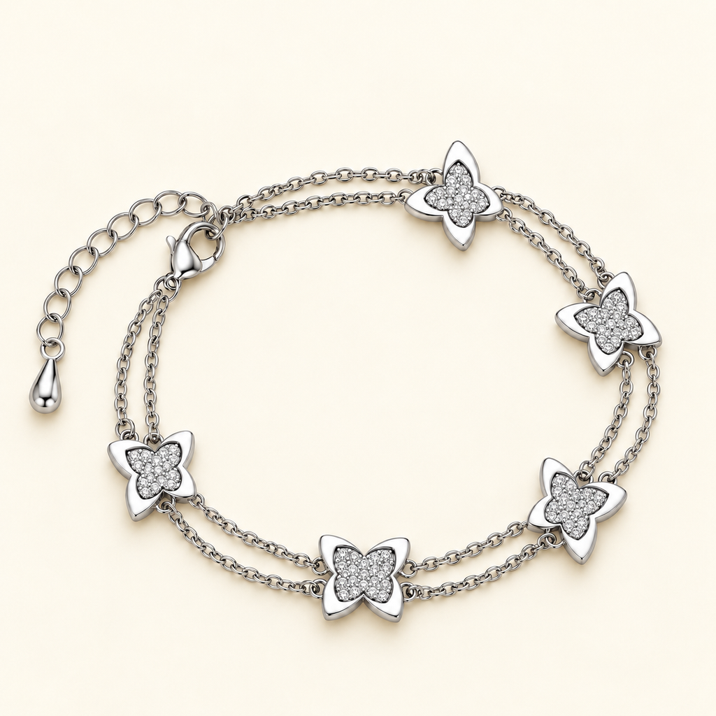 Silver-toned double-chain bracelet featuring five butterfly charms with glittery textured centres and smooth silver outlines.
Delicate layered butterfly bracelet with a lobster clasp and extension chain, displayed on a plain pink background.