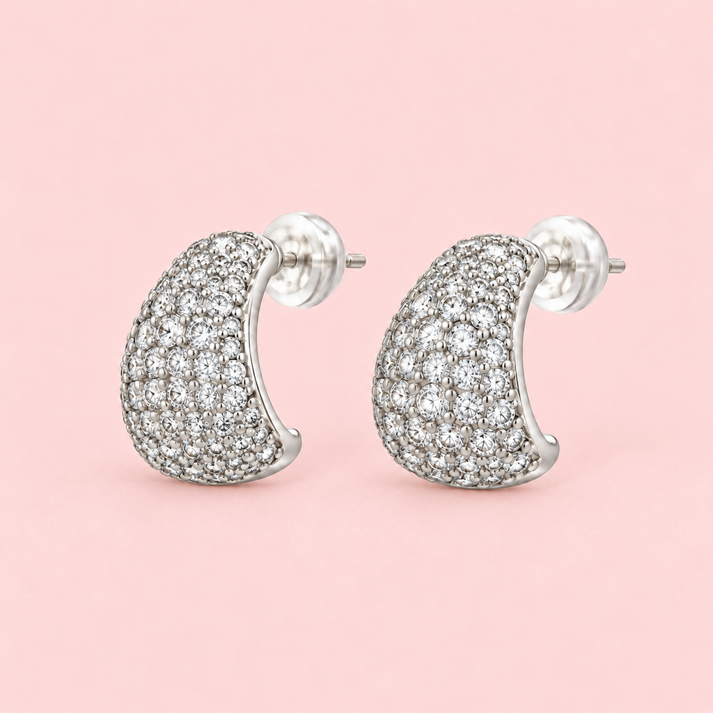 Silver-tone teardrop stud earrings with pavé-style white stones and a polished finish displayed against a pink background.