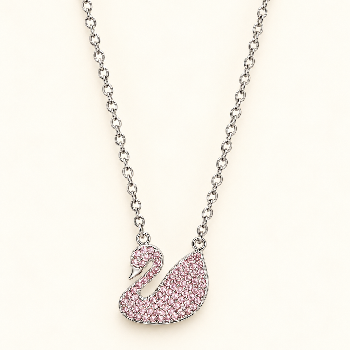 Silver-toned swan pendant necklace embellished with blush-pink sparkling stones and polished detailing.
Elegant pink swan charm suspended from a delicate silver-toned link chain against a  pink background.