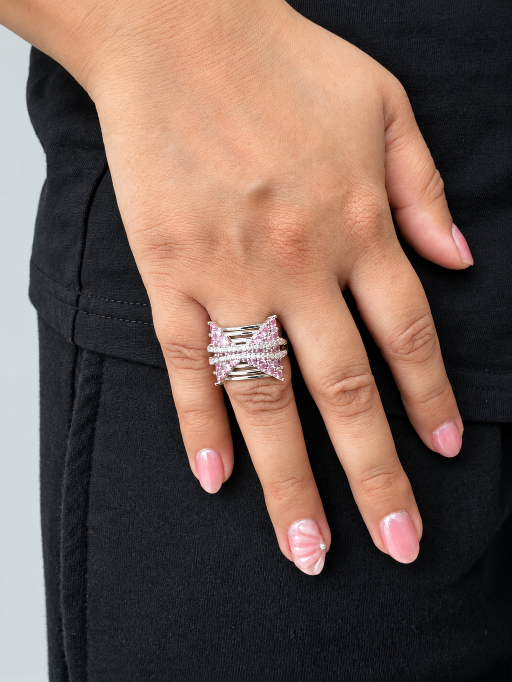A close-up of a hand wearing a silver ring with pink gemstones.