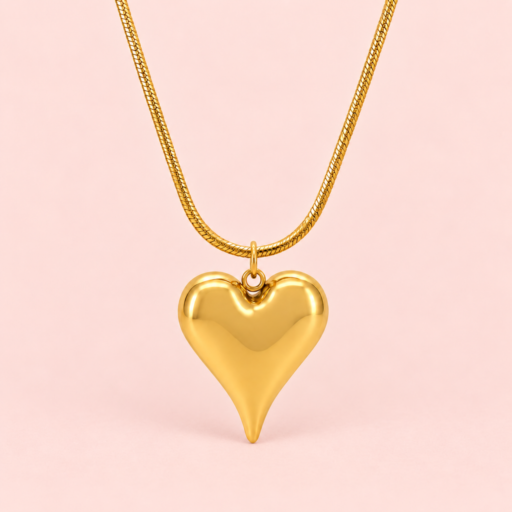 Gold-toned necklace featuring a sculpted heart pendant with a smooth polished finish and subtle black accents.

Close-up of a modern gold heart pendant on a delicate snake-style chain against a pink background.