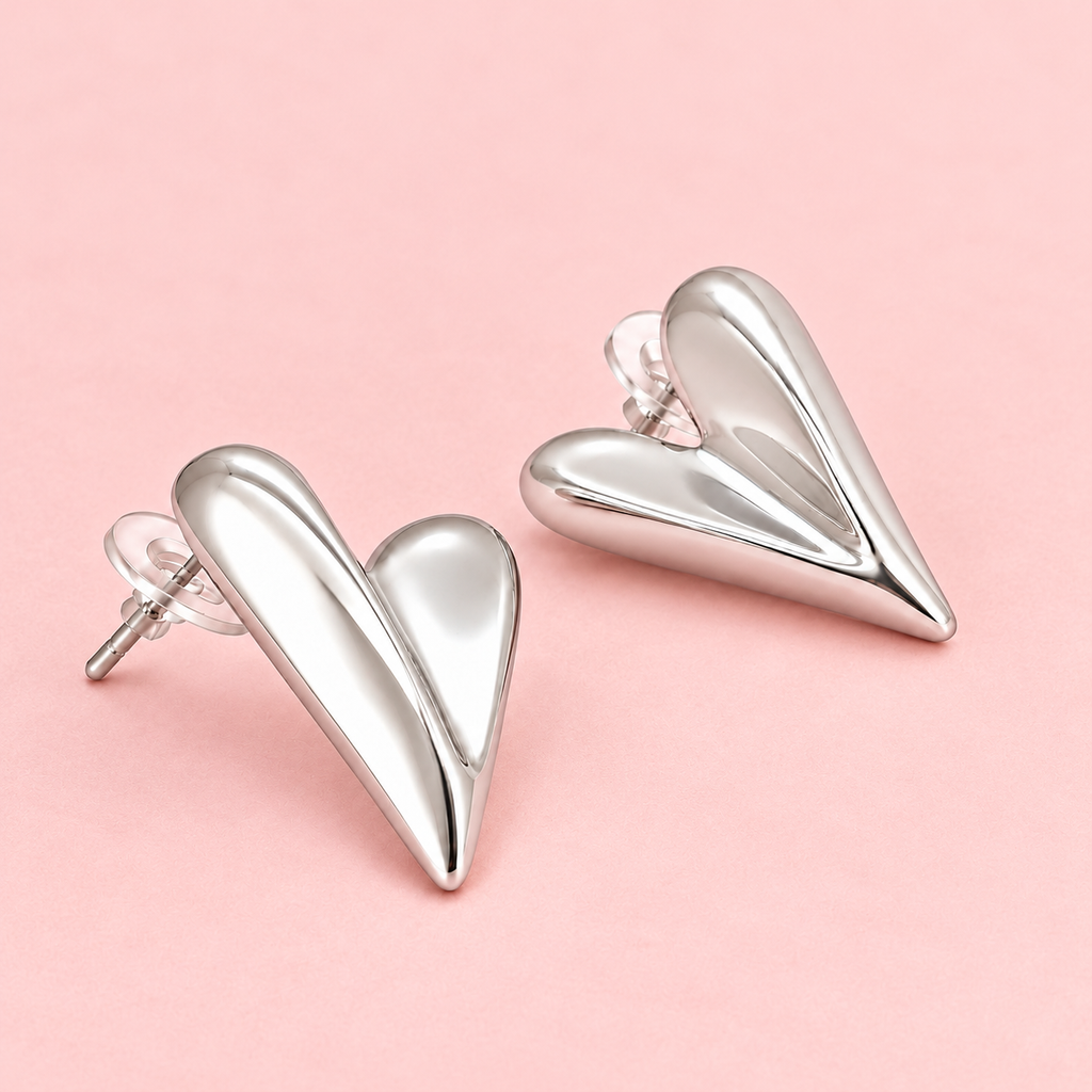 Silver-tone sculpted heart stud earrings with an abstract curved design and polished finish displayed against a pink background.