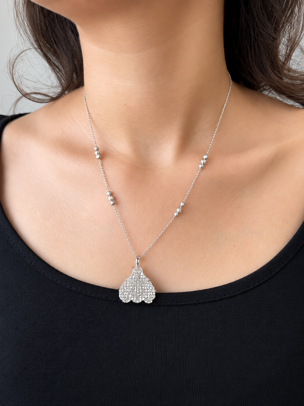 A silver pendant necklace featuring a detailed princess pendant and small silver beads on the chain, which is worn by a model wearing a black top.