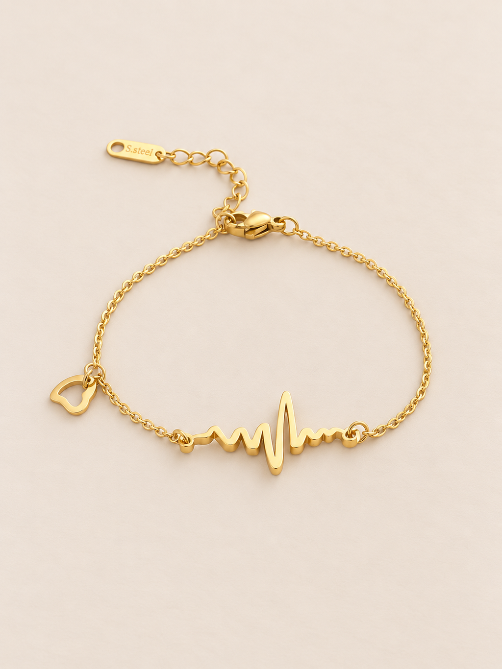 A delicate gold chain bracelet with a heartbeat line and heart charm, displayed against a pink background.