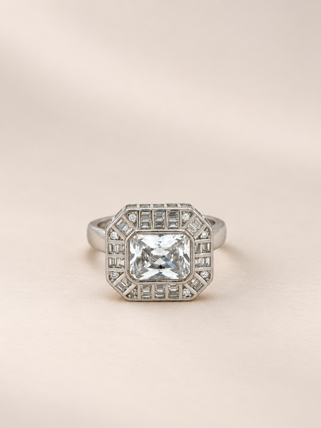 An octagonal silver ring featuring a large square clear gemstone in the center, surrounded by a double halo of smaller rectangular stones, set against a soft beige background.