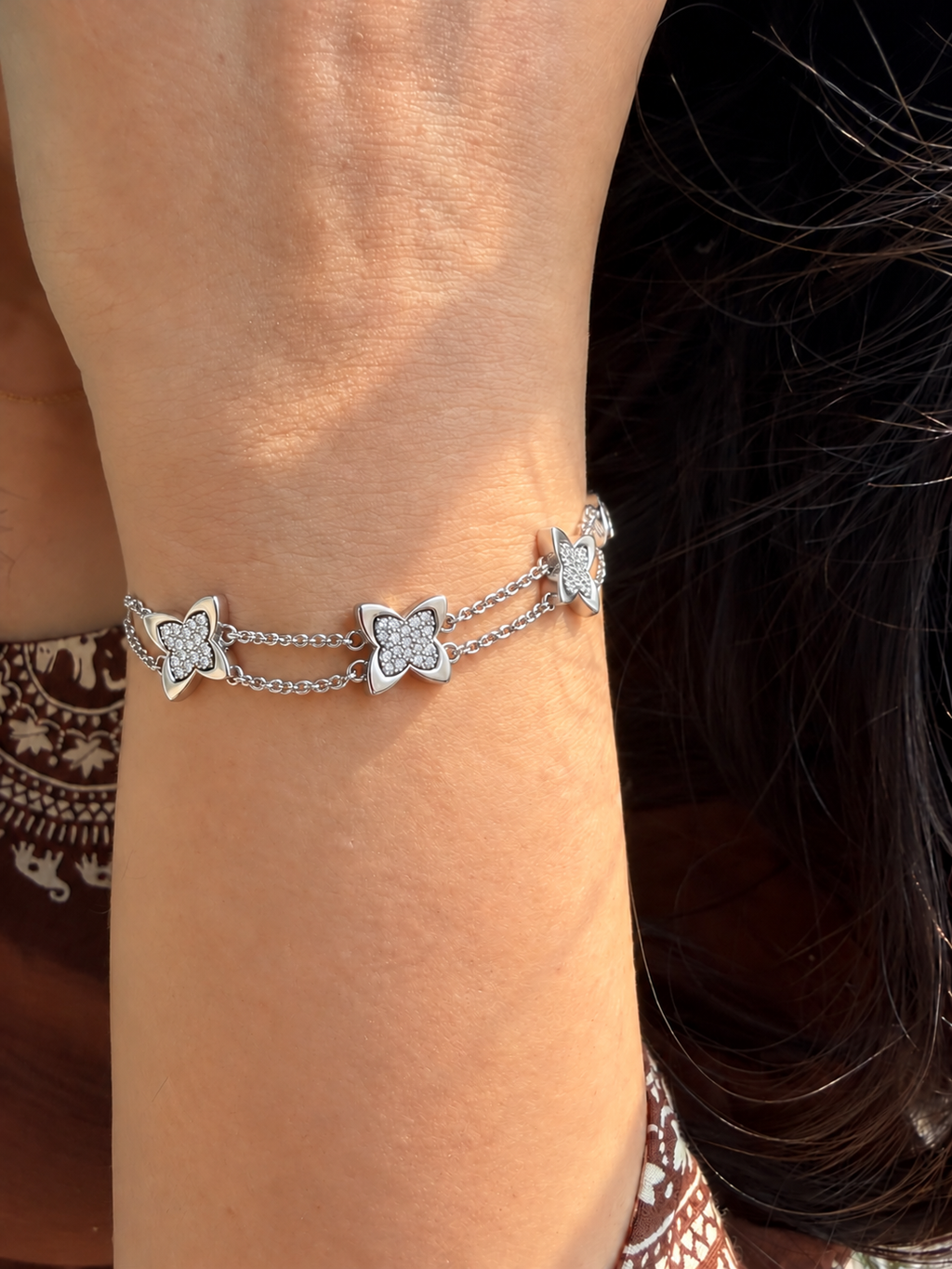 Silver-toned double-chain bracelet featuring five butterfly charms with glittery textured centres and smooth silver outlines.
Delicate layered butterfly bracelet with a lobster clasp and extension chain, worn by a model.
