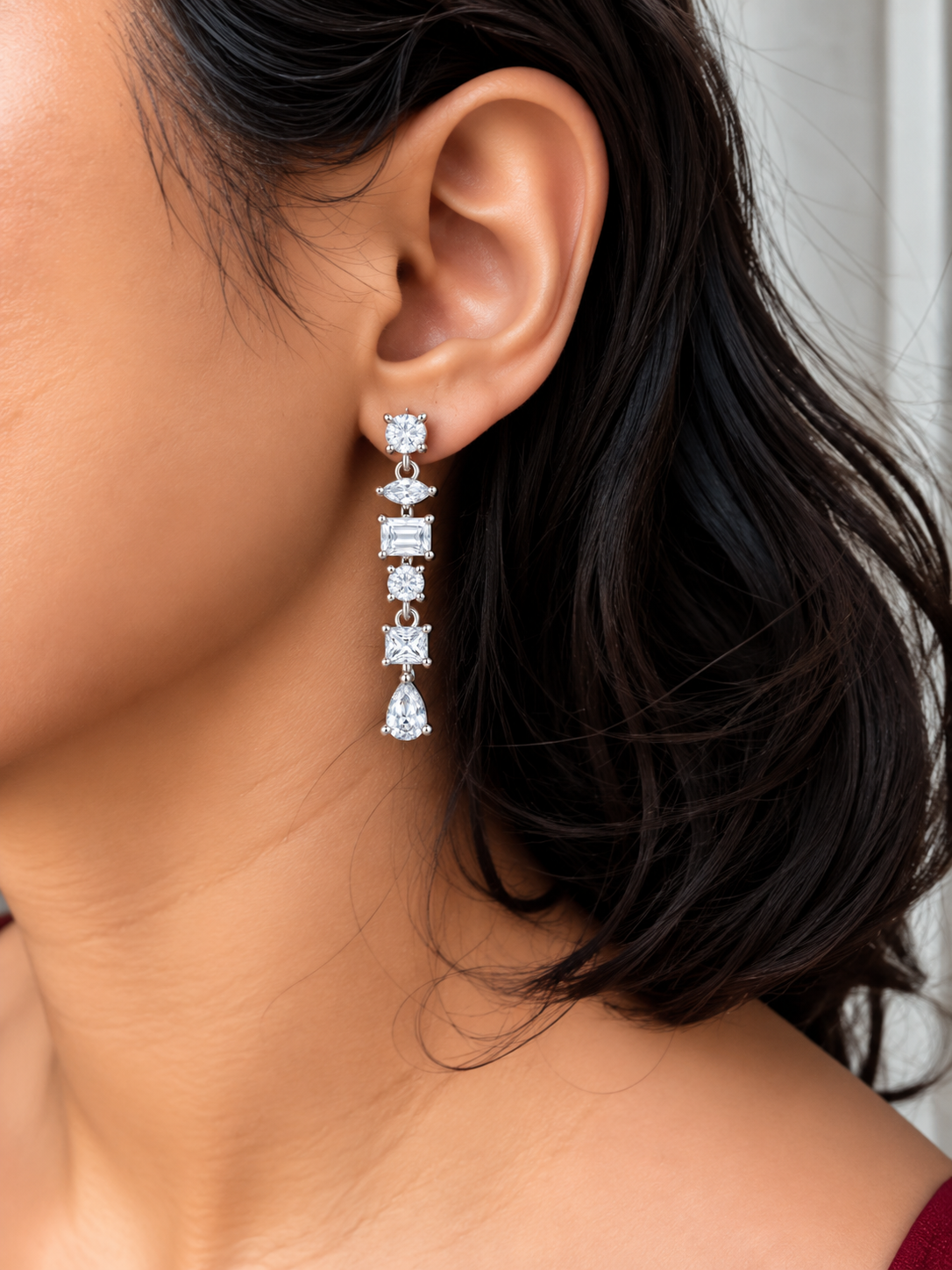 Silver-tone geometric drop earrings with round, marquise, rectangular and pear-shaped clear stones worn by a model.