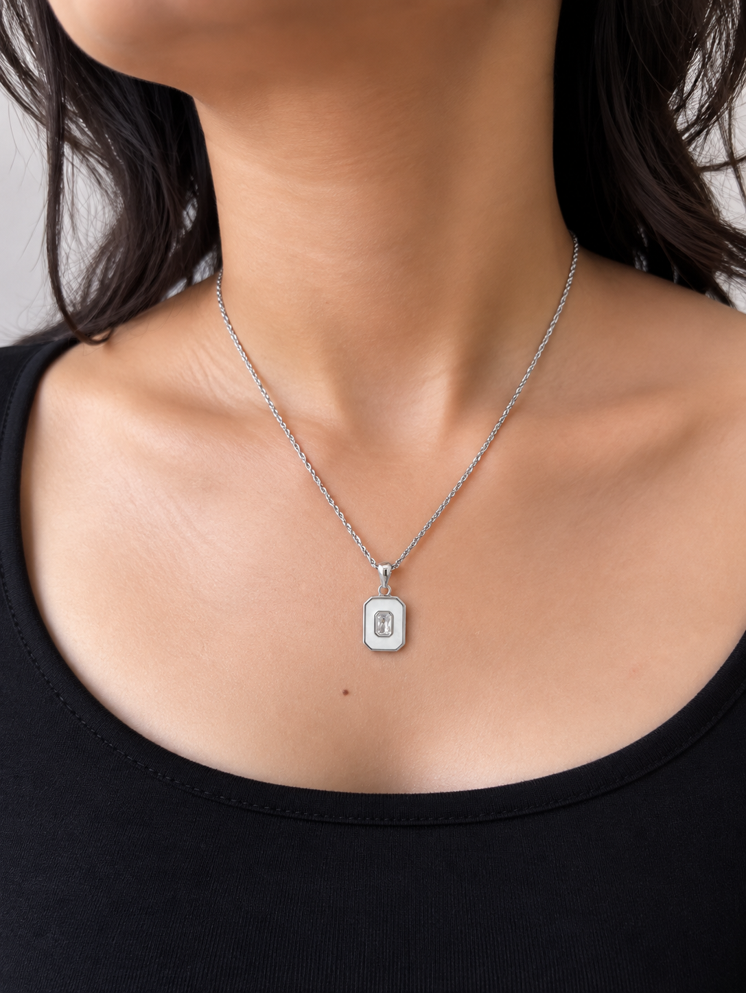 A close-up of a model wearing a silver chain necklace with a small rectangular pendant.