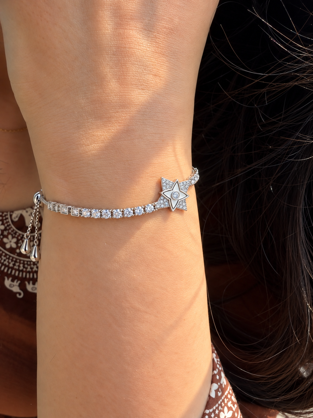 Silver-toned slider bracelet featuring a star-shaped centre motif with sparkling stone accents and a stone-studded chain.
Delicate box-link bracelet with an adjustable slider closure, worn by a model.