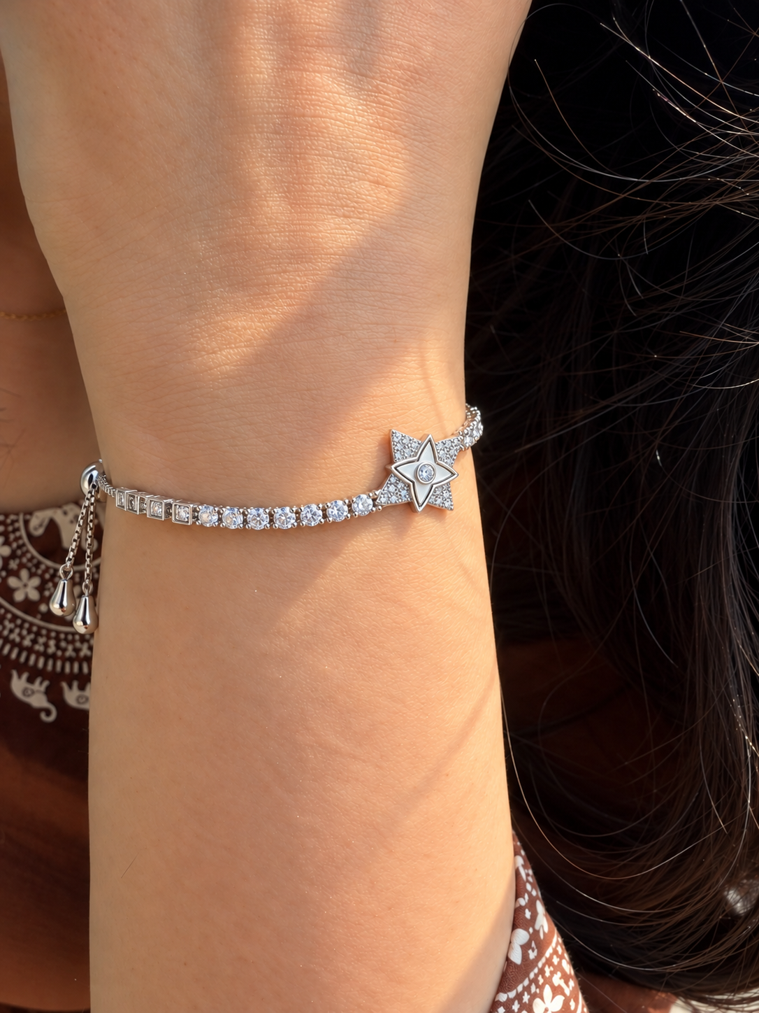 Silver-toned slider bracelet featuring a star-shaped centre motif with sparkling stone accents and a stone-studded chain.
Delicate box-link bracelet with an adjustable slider closure, worn by a model.