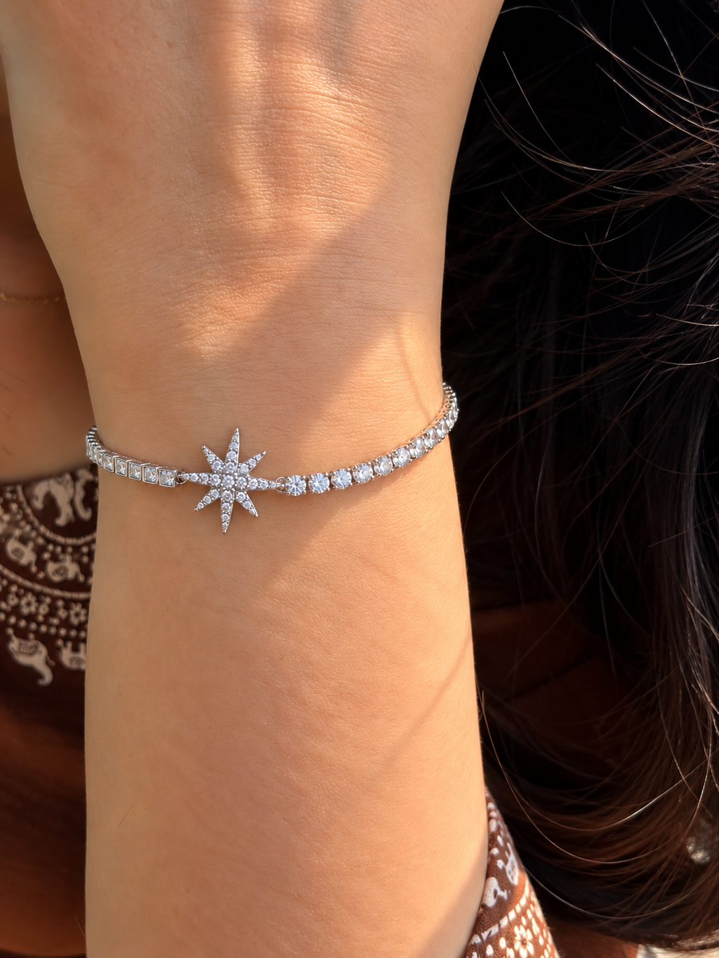 Silver-toned Celestial Starburst Bracelet featuring a multi-point star charm decorated with sparkling clear stones.
Adjustable bolo-style bracelet with round and square stone accents along the band,  worn by a model.