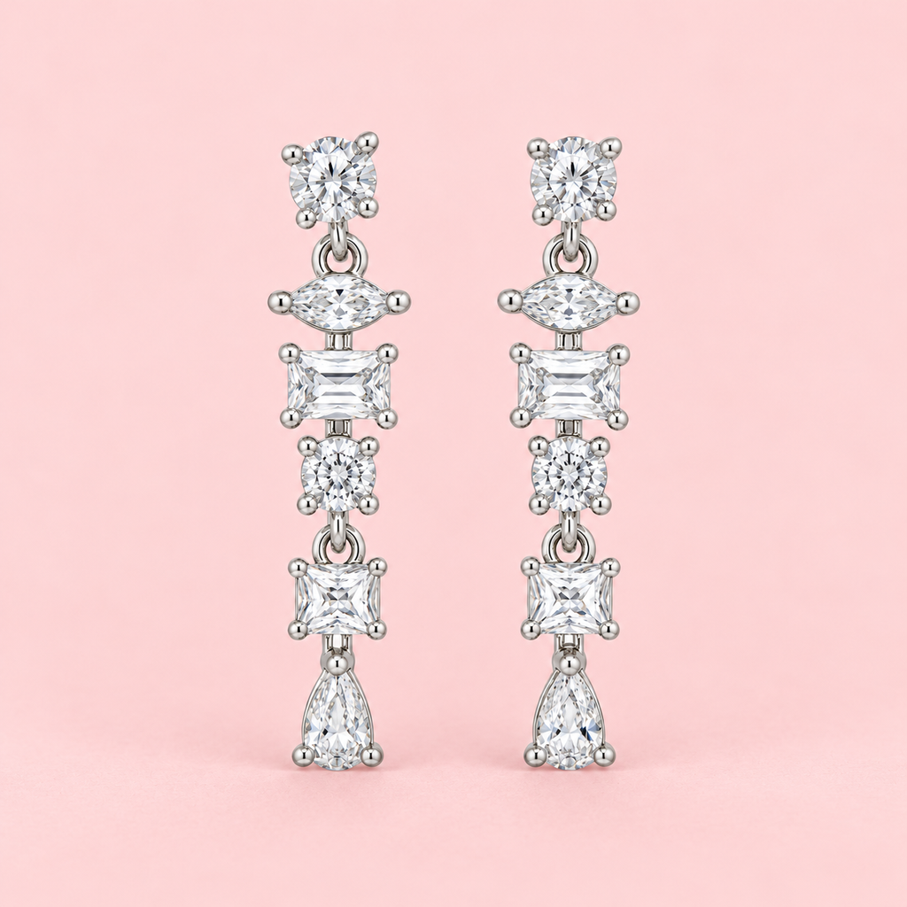 Silver-tone geometric drop earrings with round, marquise, rectangular and pear-shaped clear stones displayed against a pink background.