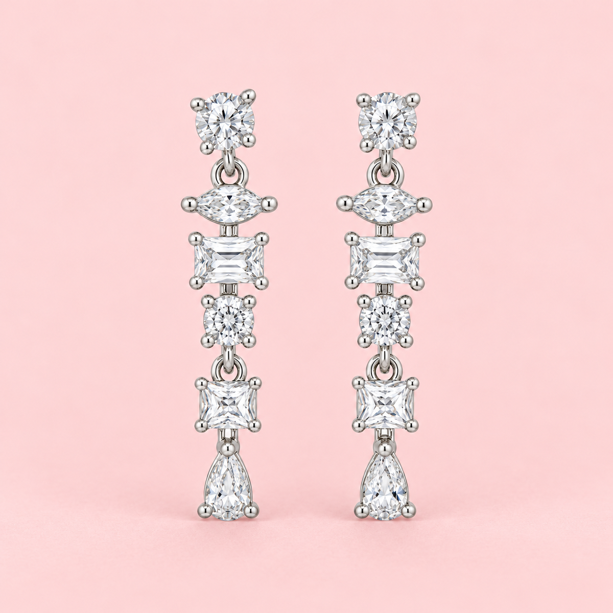 Silver-tone geometric drop earrings with round, marquise, rectangular and pear-shaped clear stones displayed against a pink background.