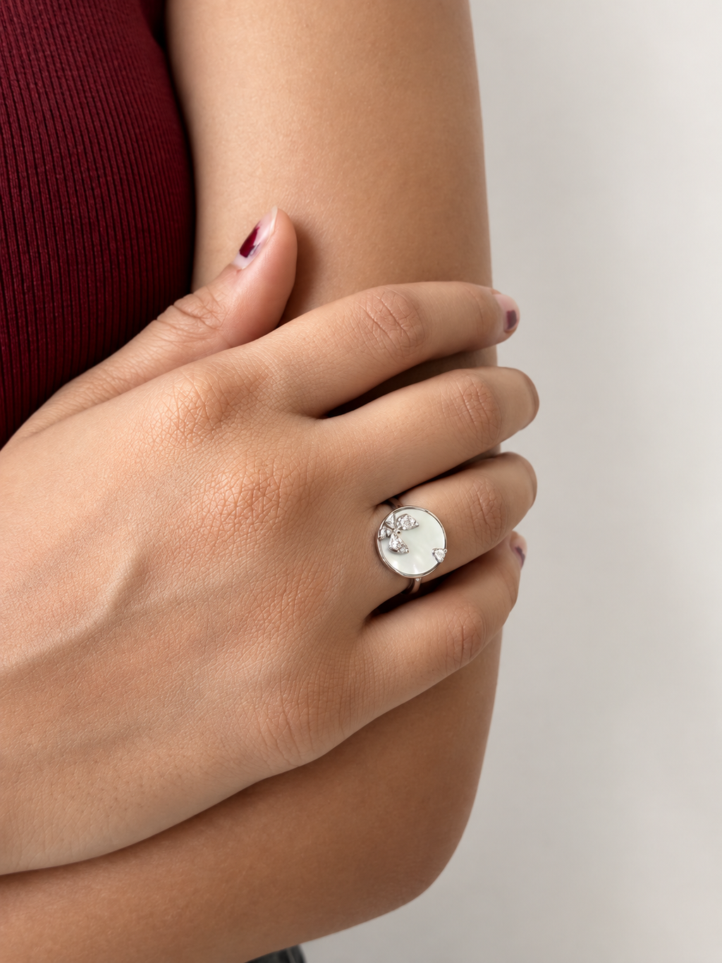 A silver ring featuring a round white mother-of-pearl inlay with a butterfly motif set with small clear crystals, wrn by a model.