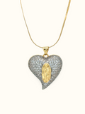 Gold-toned snake chain necklace with a heart-shaped pendant covered in clear sparkling stones and a raised golden religious figure at the centre.

Statement heart pendant necklace featuring silver-toned pavé detailing and gold accents, displayed against a white background.