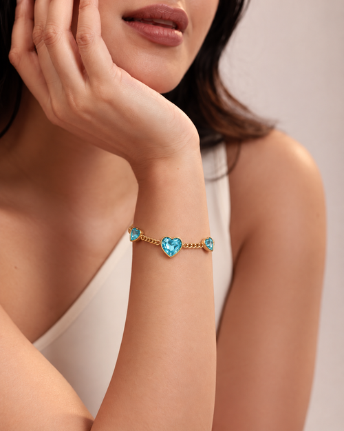 Gold chain bracelet with three heart-shaped turquoise blue crystals, worn by a model.