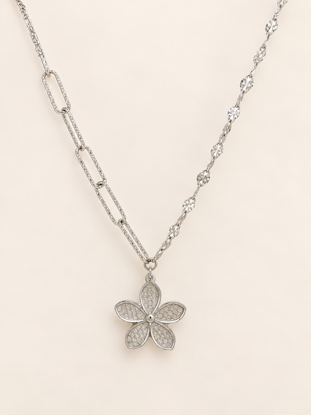 A silver-tone floral pendant necklace featuring a five-petal flower design with pavé-set clear stones, suspended from a delicate chain on a light beige background.