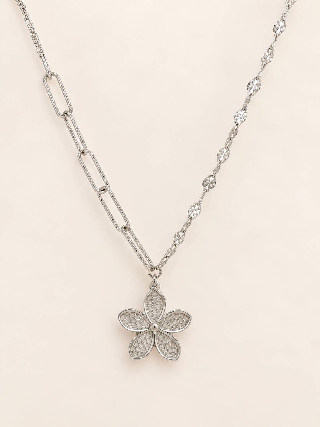 A silver-tone floral pendant necklace featuring a five-petal flower design with pavé-set clear stones, suspended from a delicate chain on a light beige background.