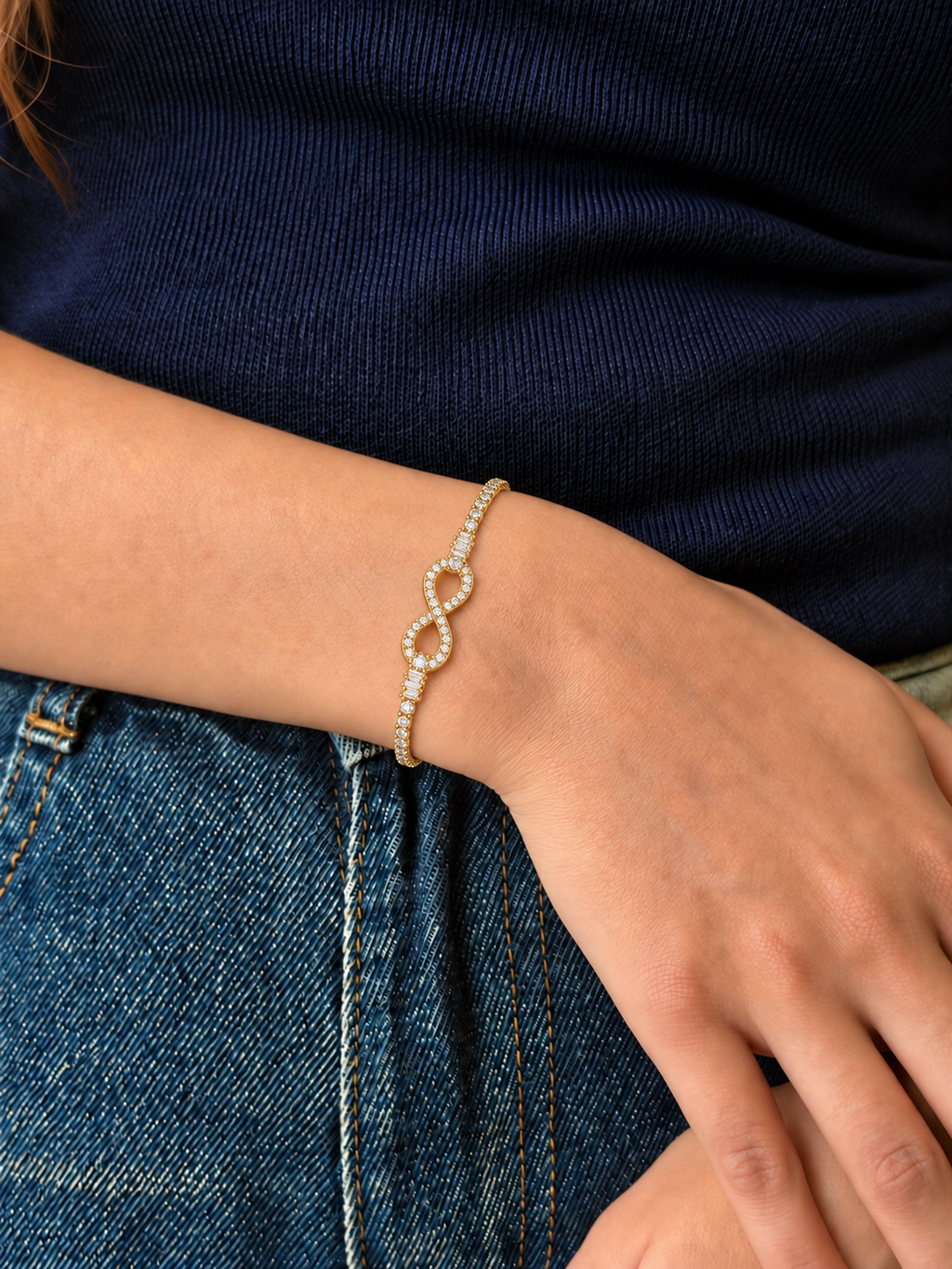A delicate gold chain bracelet with a infinity design in the middle filled with diamonds and both sides has circle diamonds worn by a model.