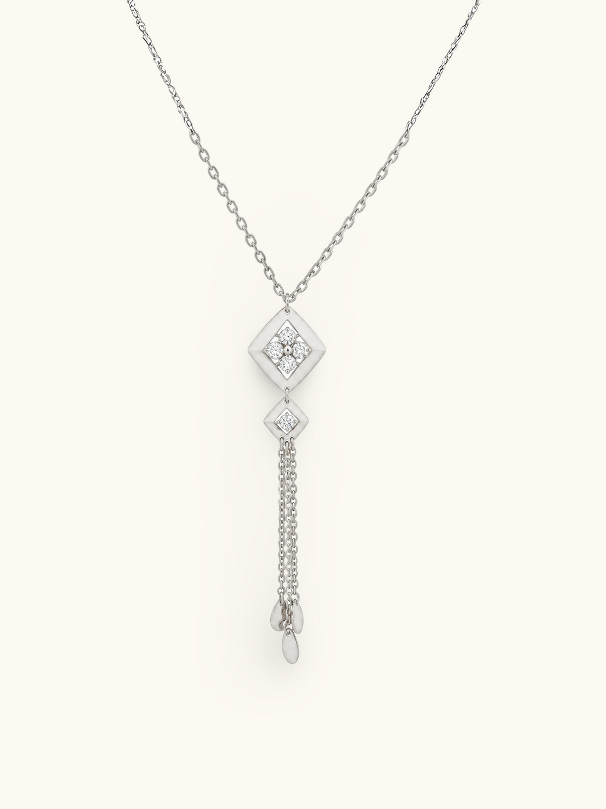 A silver-toned dangle necklace featuring a diamond-shaped pendant set with clear stones, a smaller matching pendant, and two dangling chain drops with teardrop charms, shown on a plain off-white background.