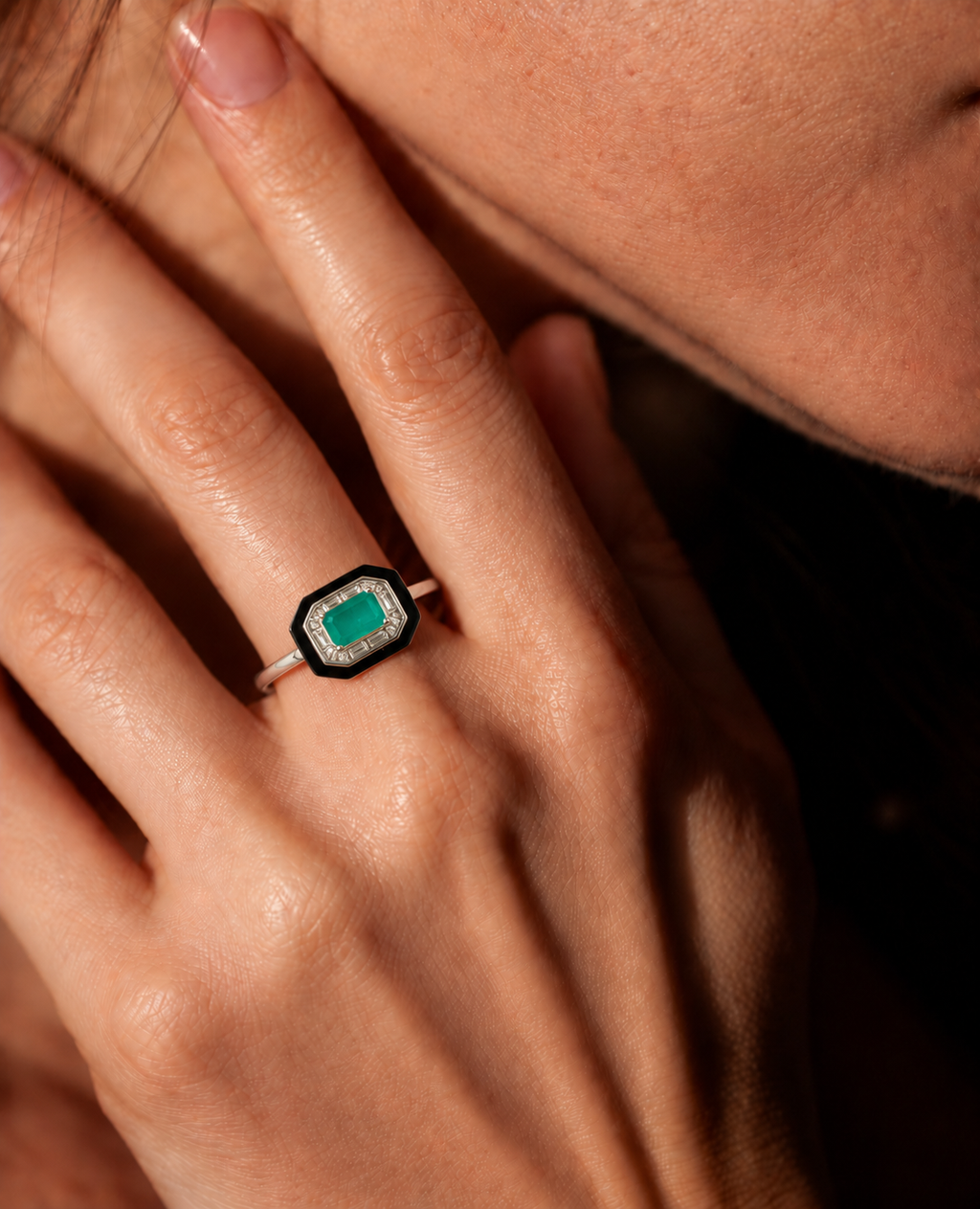 An octagonal ring featuring a vibrant emerald green center stone surrounded by a black and silver geometric border, set on a silver band worn by a model.