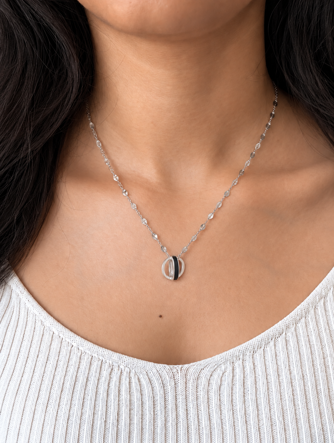 A close-up of a model wearing a delicate silver chain necklace with a small circular pendant featuring a black and white interlocking circle design.
