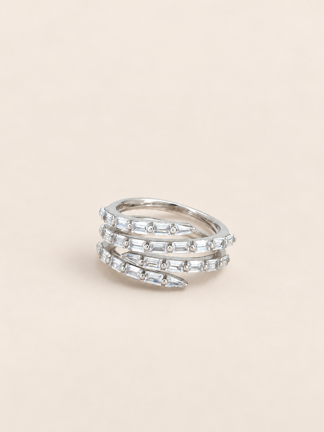 A silver wrap ring adorned with clear baguette and round-cut stones, presented on a solid light beige background.