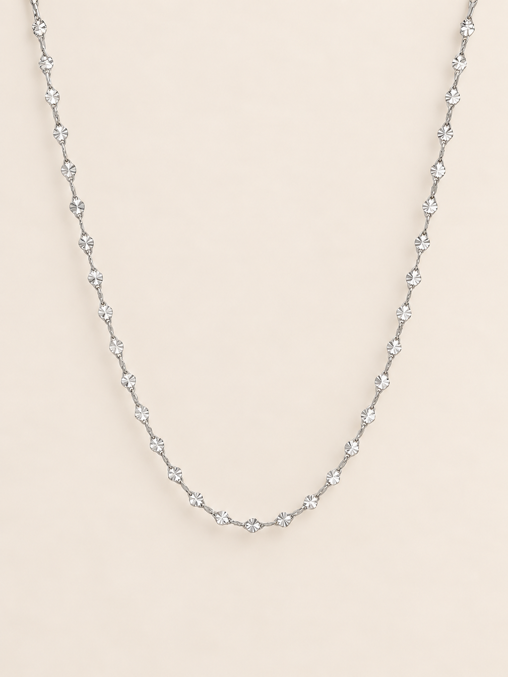A delicate silver twisted simple chain, displayed against a solid pale beige background.