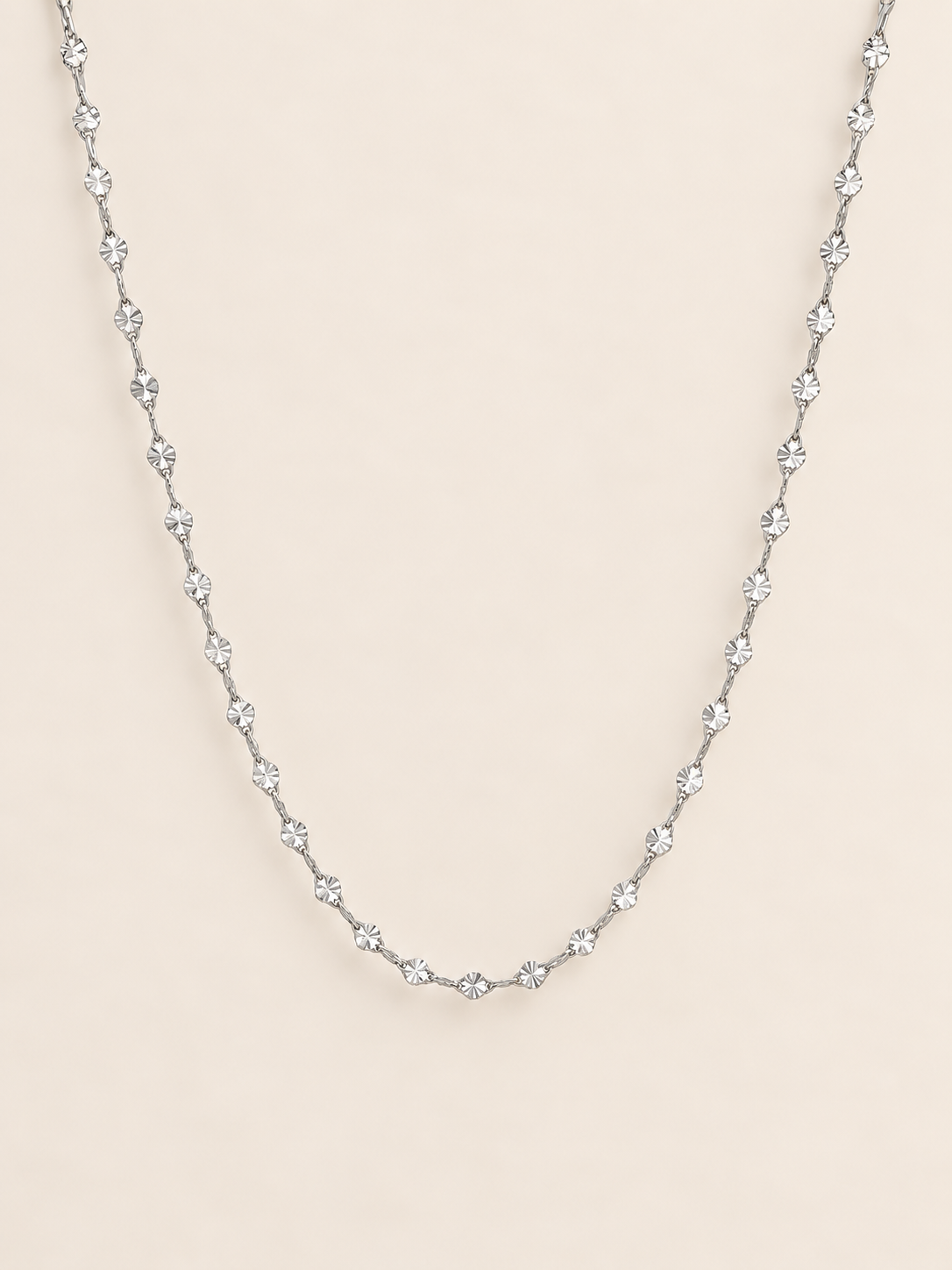 A delicate silver twisted simple chain, displayed against a solid pale beige background.