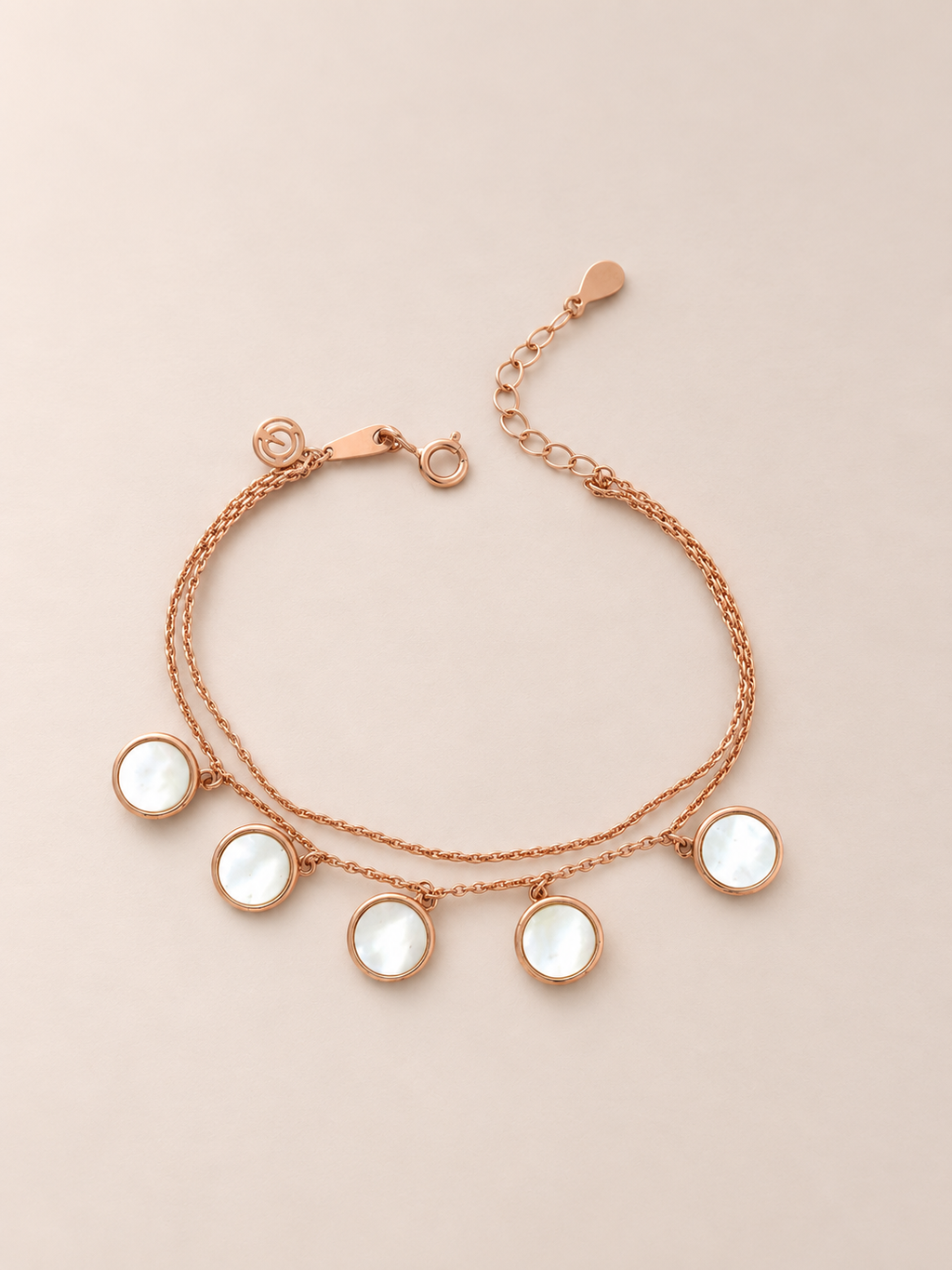 A rose gold double-strand bracelet featuring five round, bezel-set white mother-of-pearl pendants, displayed on a solid beige background.