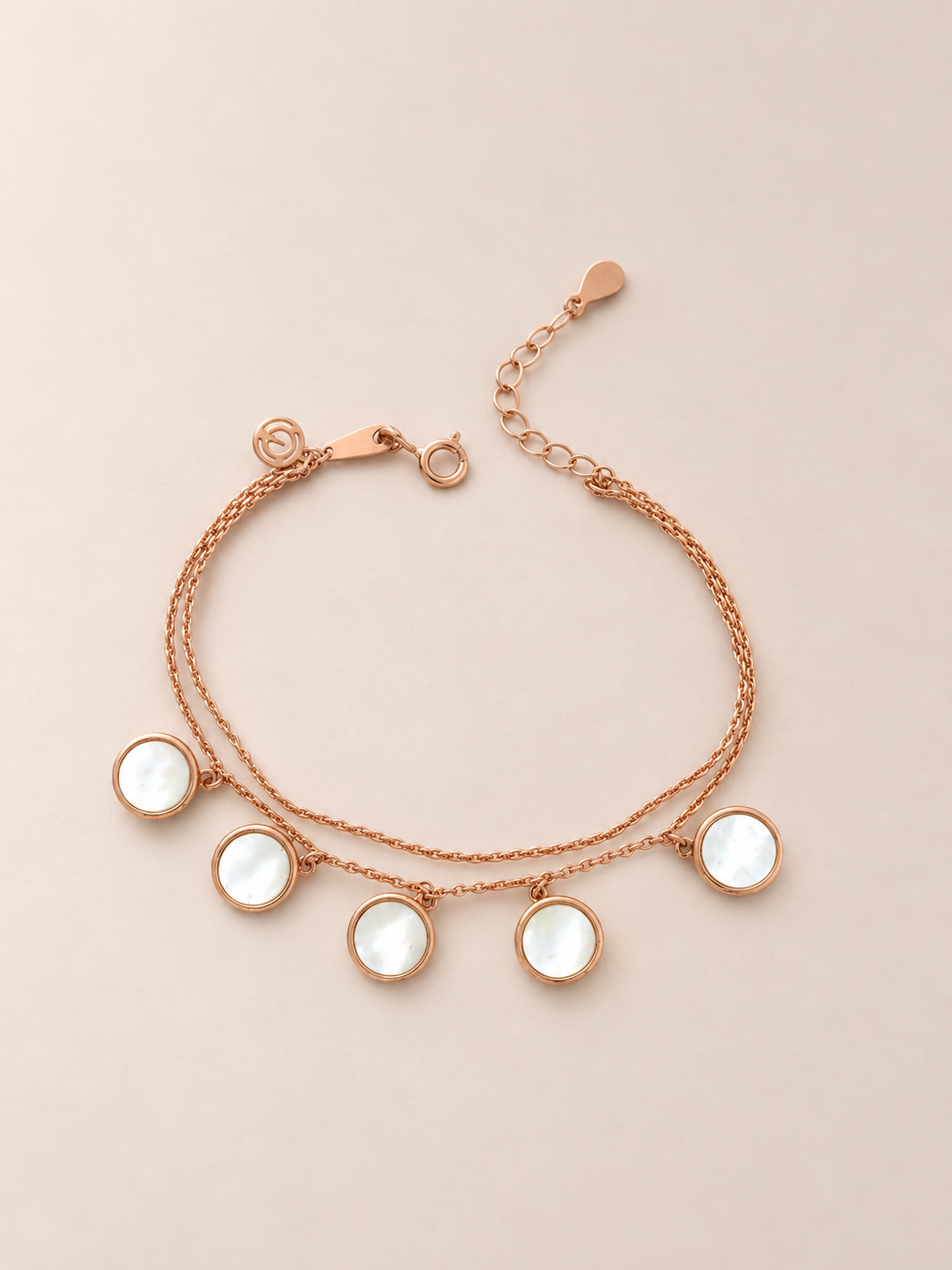 A rose gold double-strand bracelet featuring five round, bezel-set white mother-of-pearl pendants, displayed on a solid beige background.