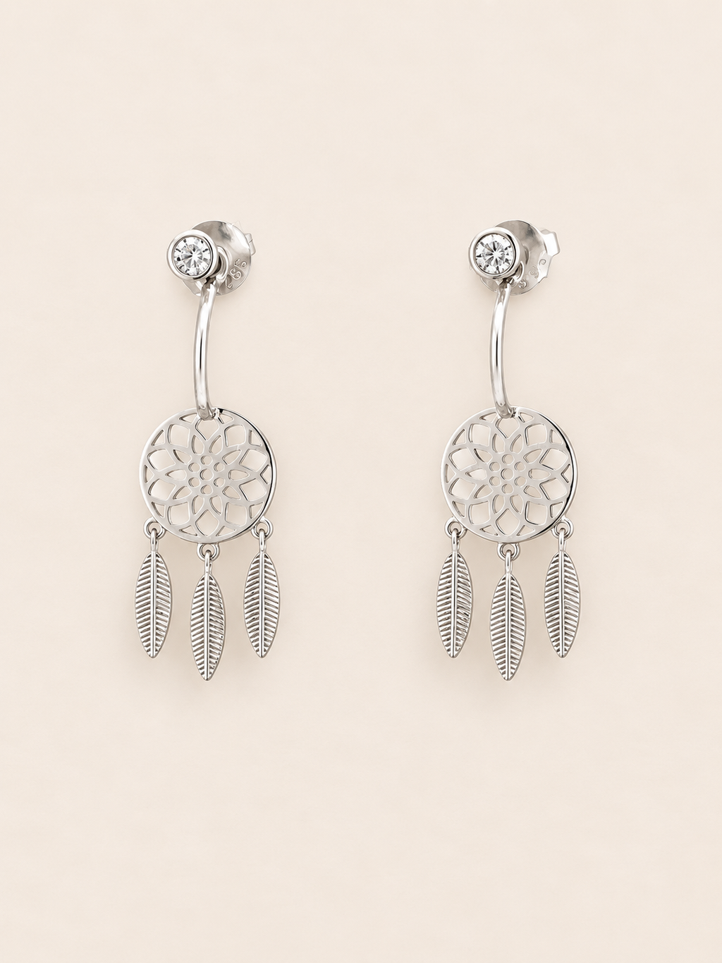 A pair of silver dreamcatcher stud earrings with a small clear crystal in the center of each, hanging from curved posts with three dangling feather charms each, set against a solid pale beige background.