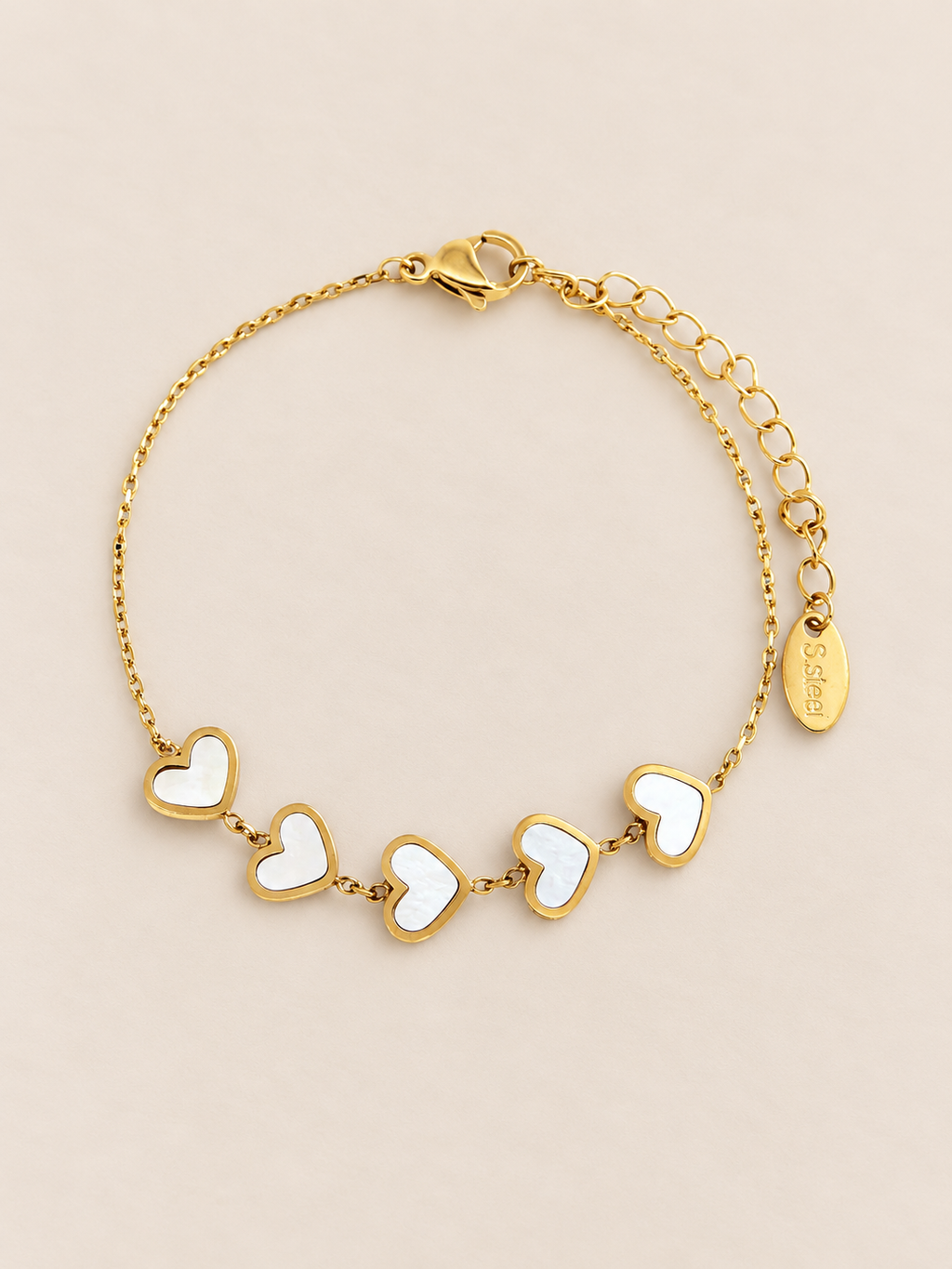 A golden chain bracelet with hearts and a lobster clasp and extender chain, displayed on a light beige background.