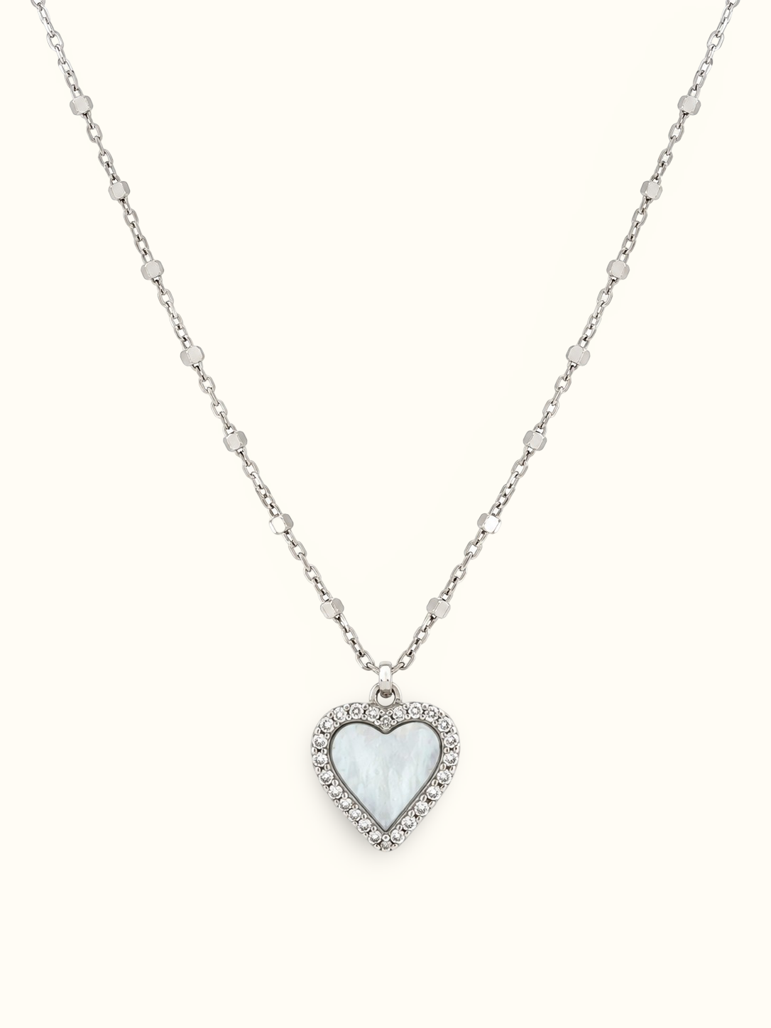 A silver heart pendant necklace featuring a milky white mother-of-pearl heart inlay, surrounded by a halo of small clear crystals on a delicate silver chain, set against a solid off-white background.