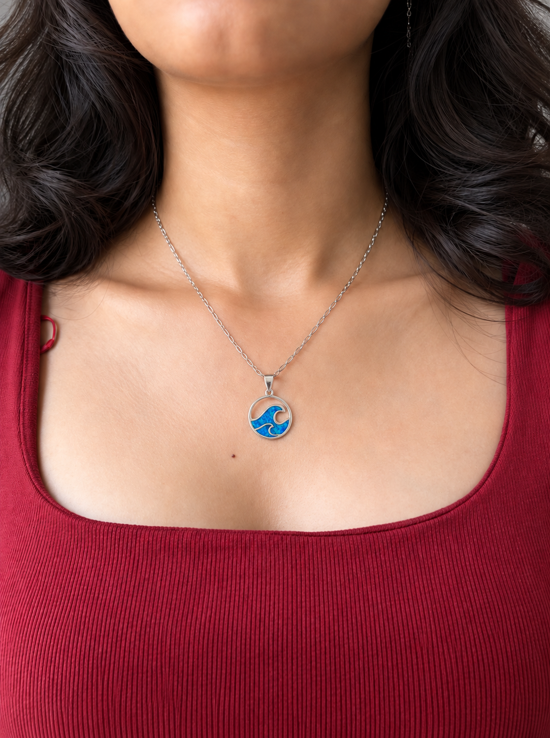 A silver chain necklace with a circular pendant featuring a blue and white wave design, worn by a model.