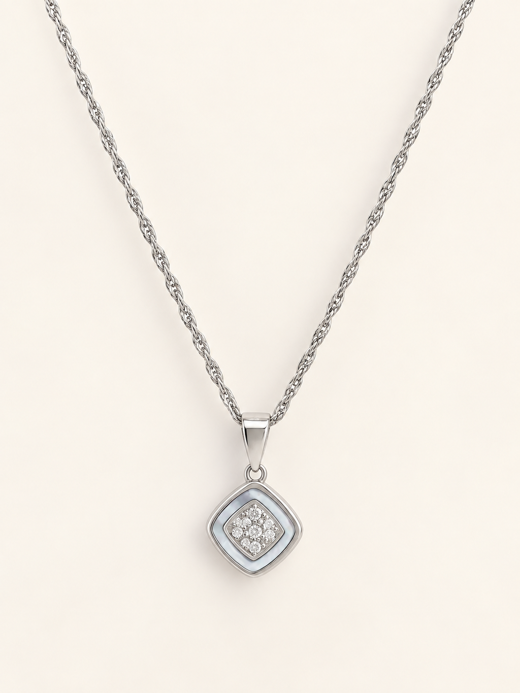 A silver rope chain necklace with a square pendant featuring a silver border and a central cluster of small clear stones, displayed on a light cream background.