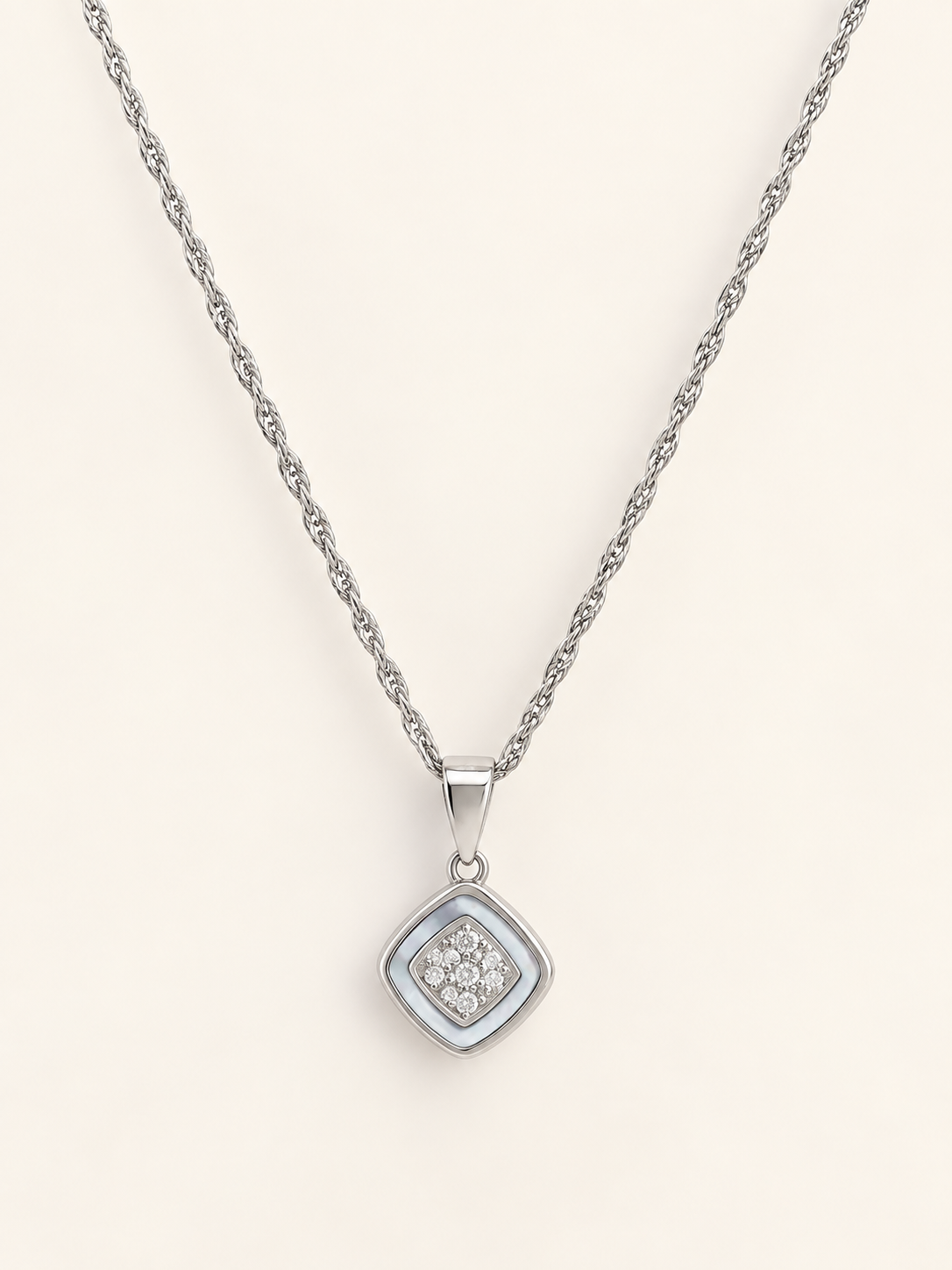 A silver rope chain necklace with a square pendant featuring a silver border and a central cluster of small clear stones, displayed on a light cream background.