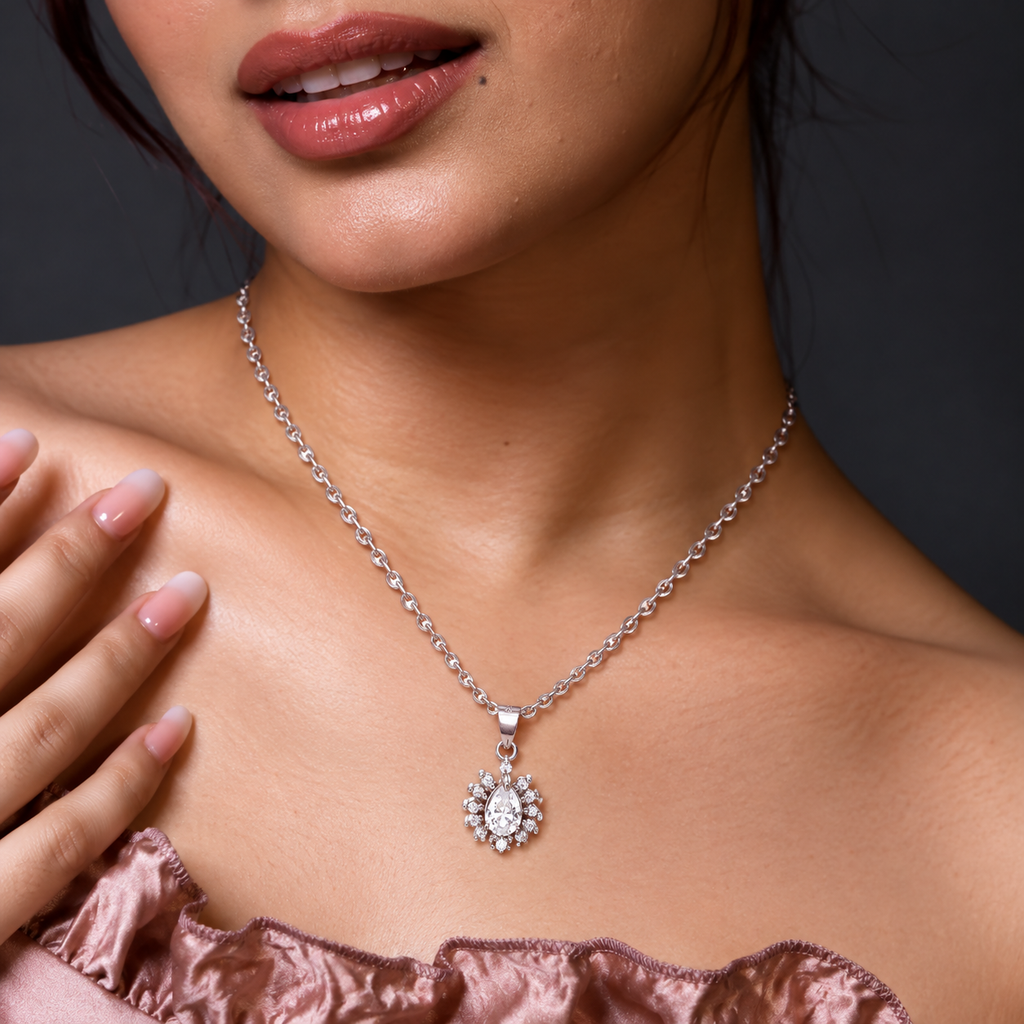 A silver-tone chain necklace with a sunburst pendant featuring a pear-shaped clear gemstone and small surrounding stones, worn by the model.