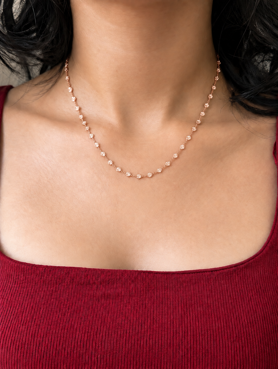 A delicate rose gold chain necklace worn by a model in a red ribbed top.