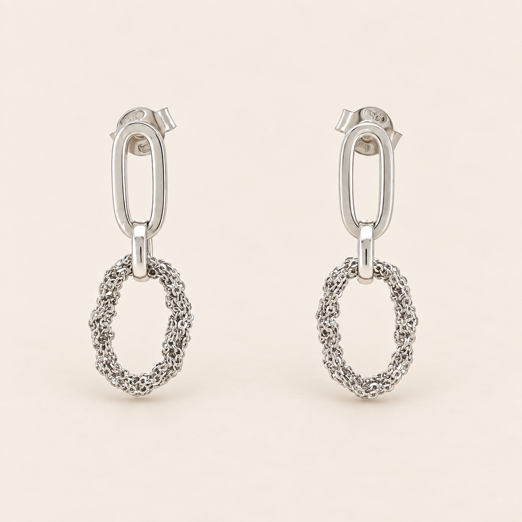 A pair of silver drop earrings with a polished oval post and a textured, openwork oval dangle, shown on a light beige background.